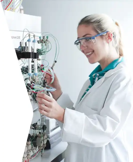 A smiling woman with safety goggles and a lab coat works with a high-quality YMC device.